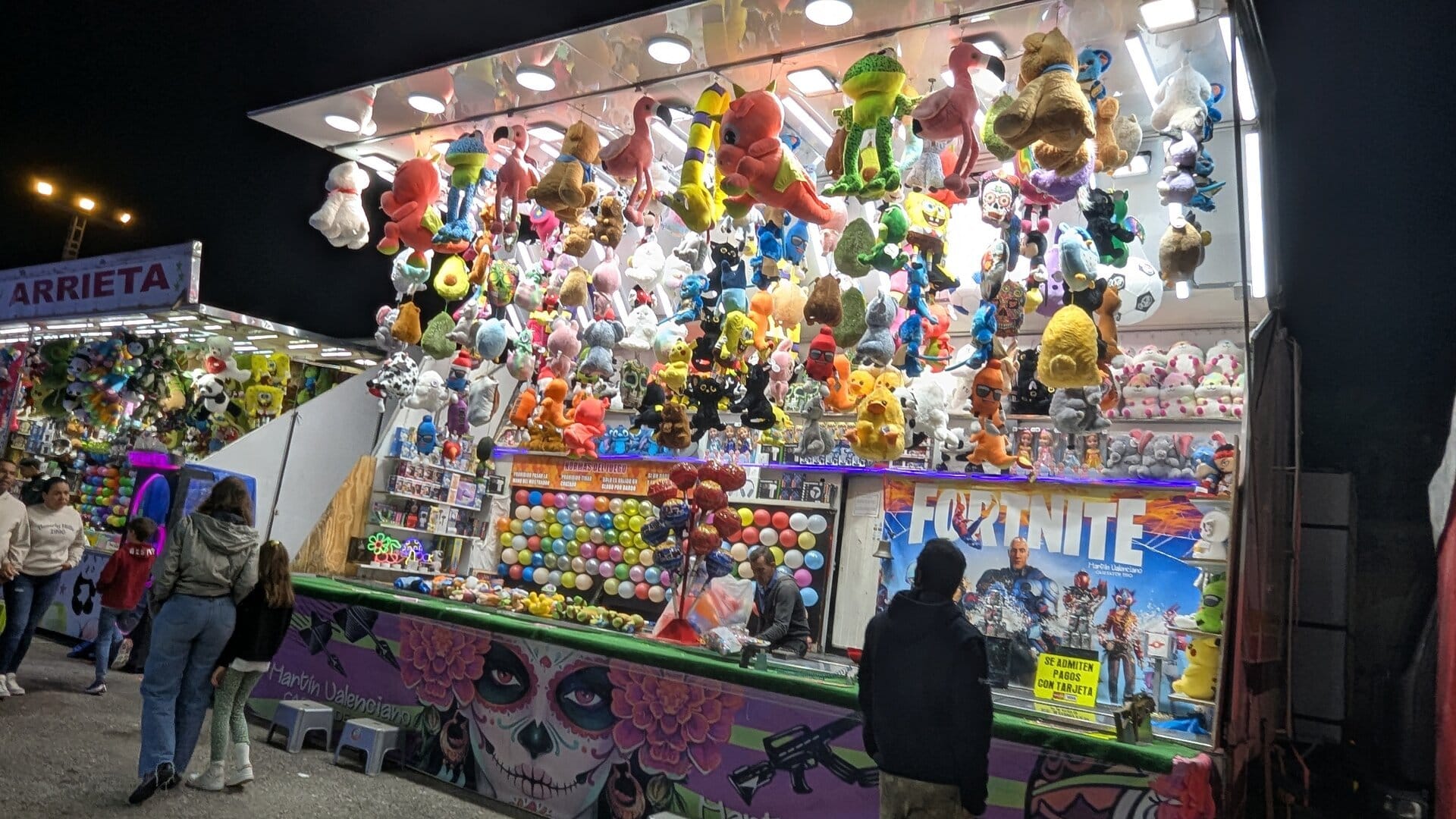 Caseta de dardos a globos de Martín Valenciano, con mural de catrina, panel de Fortnite y el cartel de normas del juego