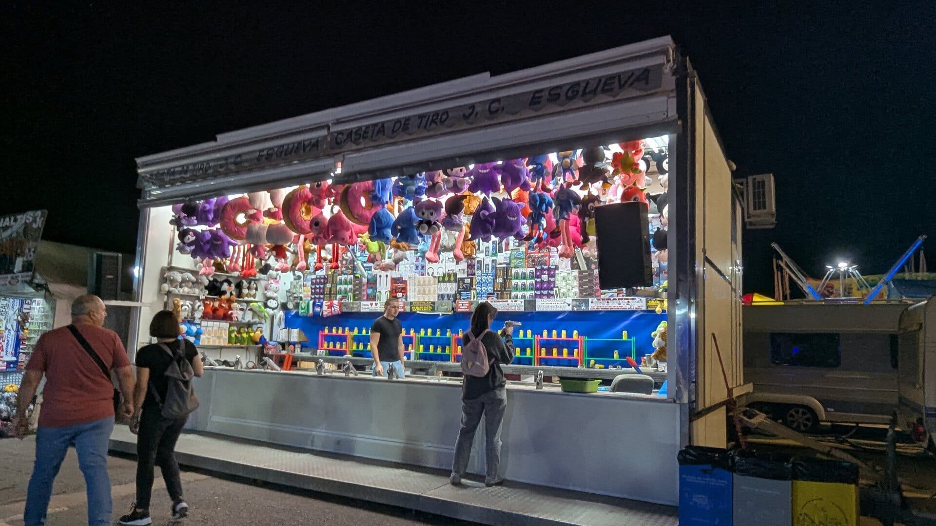 Caseta de tiro J. C. Esgueva en la Feria de Todos los Santos de Dénia, con las hileras de botes de colores como diana y los peluches colgados del techo
