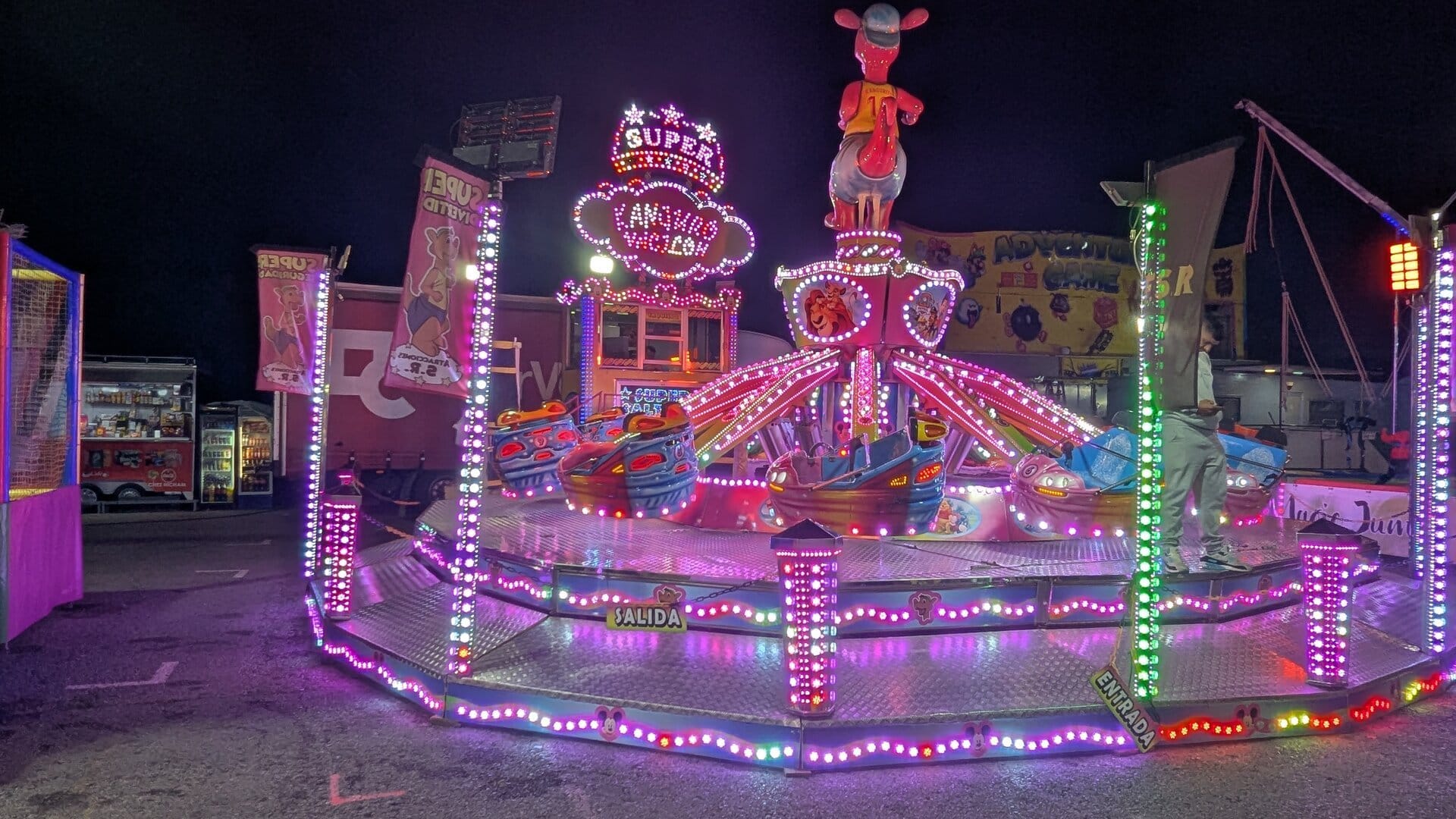 La atracción Super Kanguro Volador de la feria de Dénia, con el canguro iluminado sobre el techo y las señales de entrada y salida