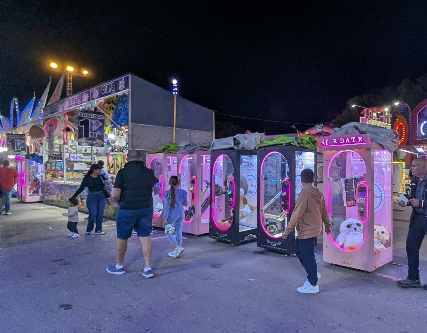 Fila de máquinas de garra Pikdate iluminadas en rosa, con peluches y patinetes en su interior