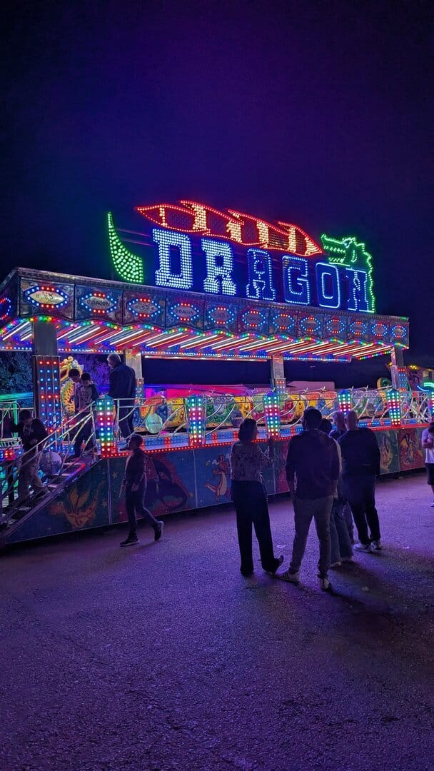 La atracción Dragon de la feria de Dénia, una montaña rusa infantil con el rótulo iluminado en azul y rojo