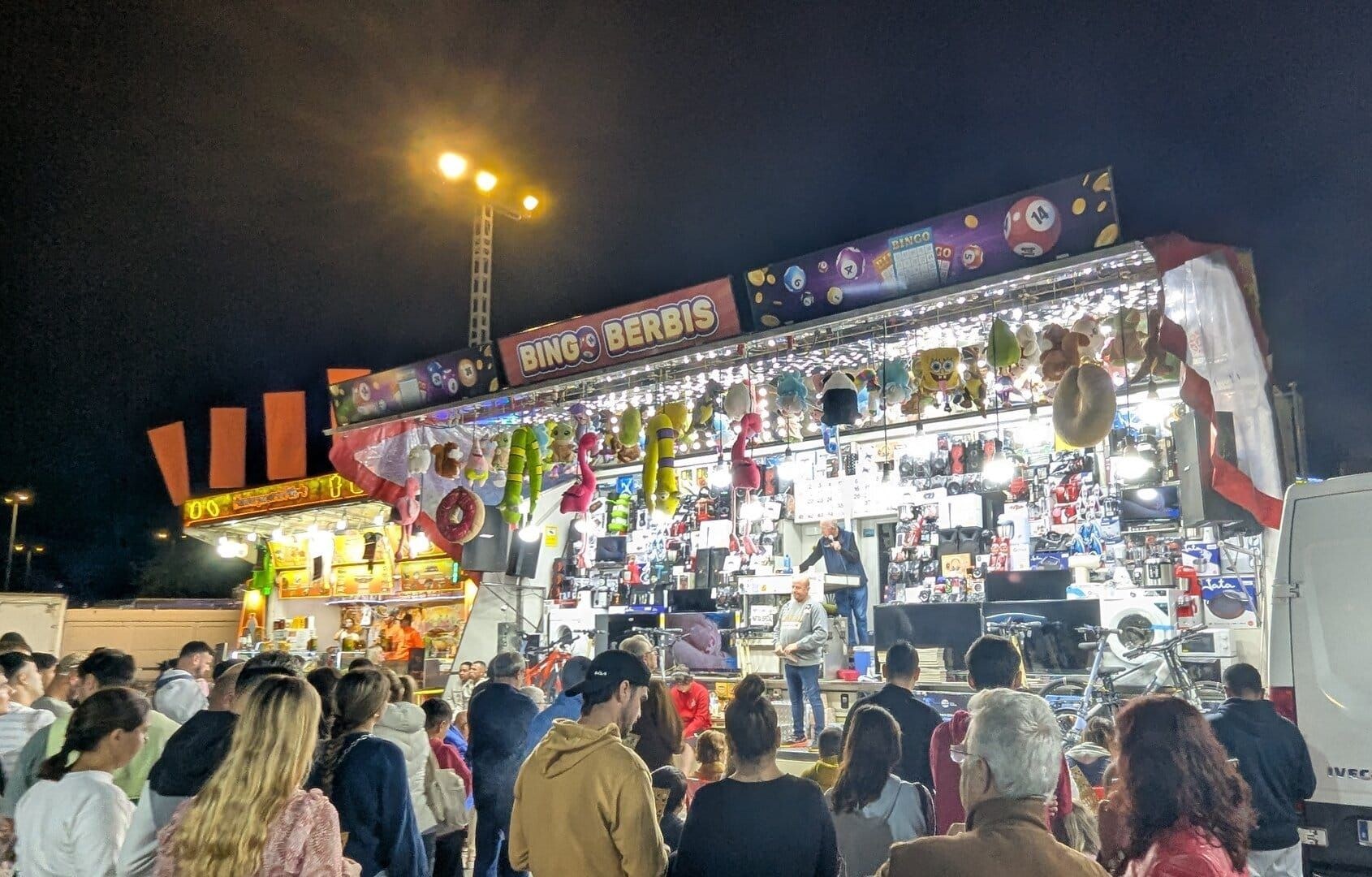 Bingo Berbis en la Feria de Todos los Santos de Dénia, con el locutor al micrófono y electrodomésticos, bicicletas y una lavadora como premios