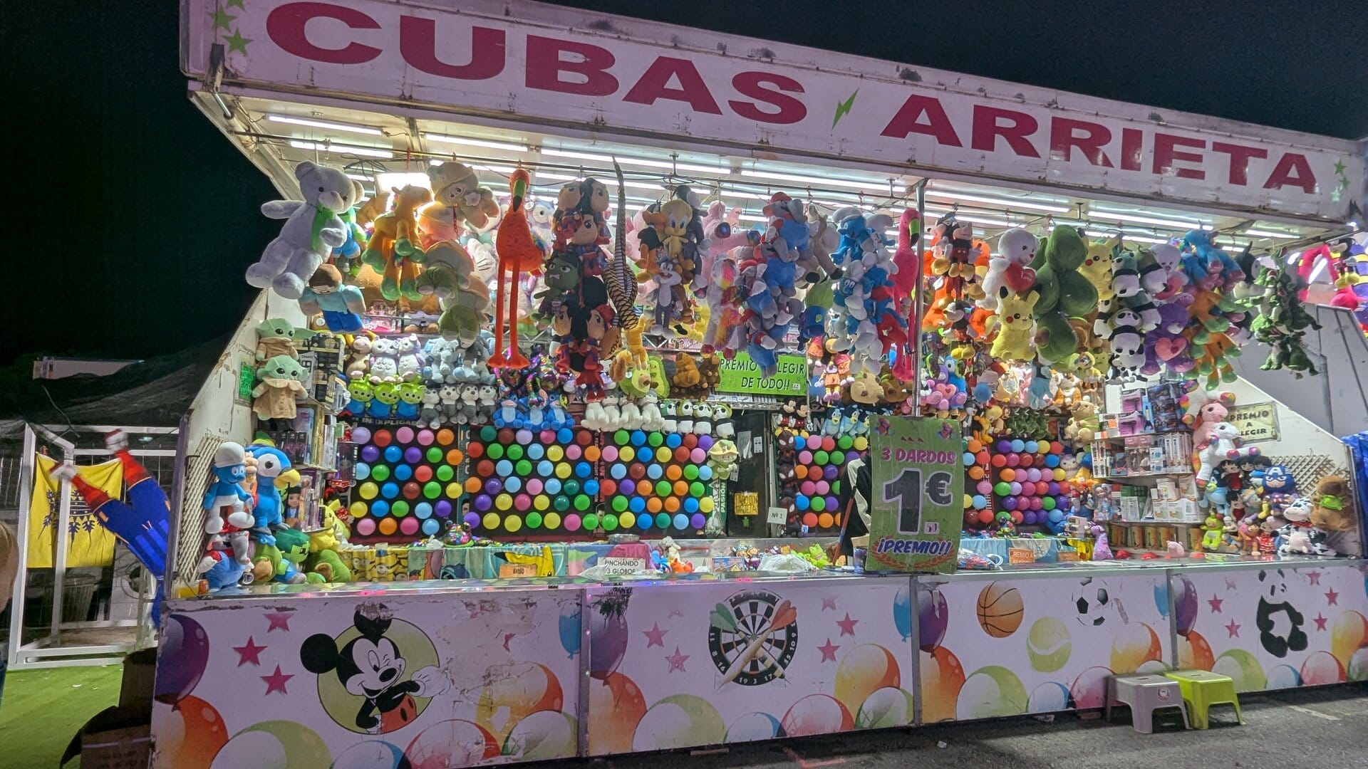Caseta Cubas Arrieta con el cartel de 3 dardos por 1 euro y premio a elegir, y la pared de globos de colores